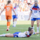 Ella Toone celebrates her goal by lying on the pitch with her arms extended like she is flying.