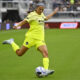 Ashley Hatch, in a yellow jersey, kicks the ball in a match against the Portland Thorns