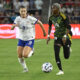 Two players chase after a ball on a soccer field