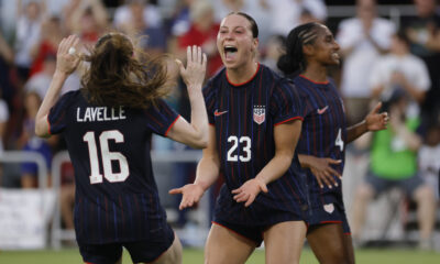 Two players celebrate on the field in blue jerseys after a goal is scored