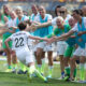 USWNT defender Meghan Klingenberg runs down the sideline, high-fiving teammates. She is facing away from the camera.